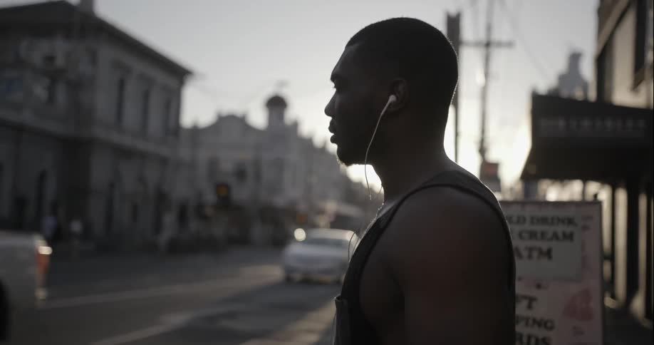 A man is standing near a street wearing earbuds