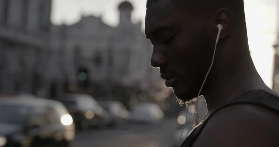 Man wearing earphones looks at his phone in the cit