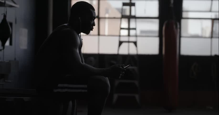 A man is sitting in a dark gym listening to music on his phone