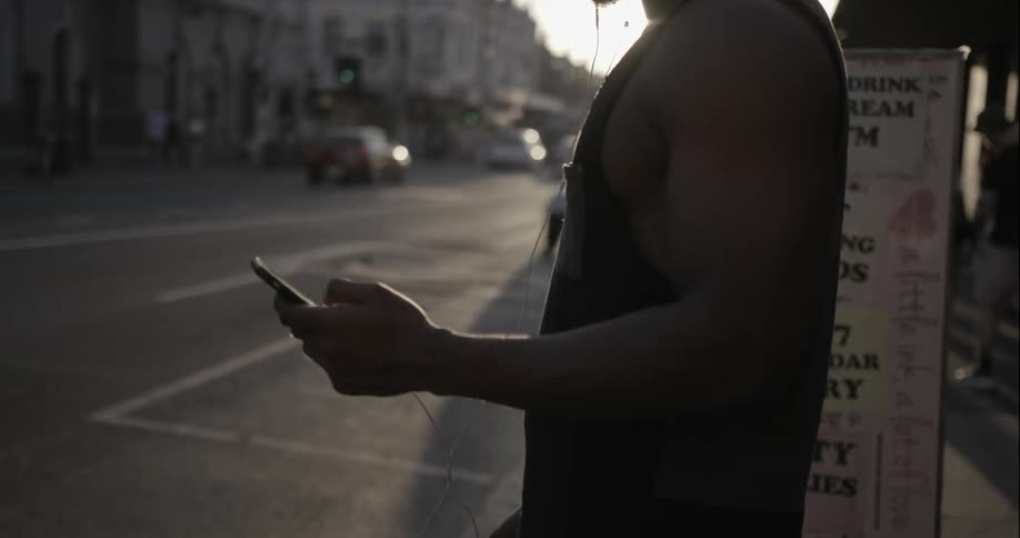 A man is using his phone standing on a sidewalk