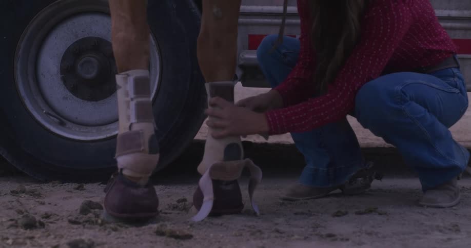 Cowgirl adjusting boots on her horse at morning