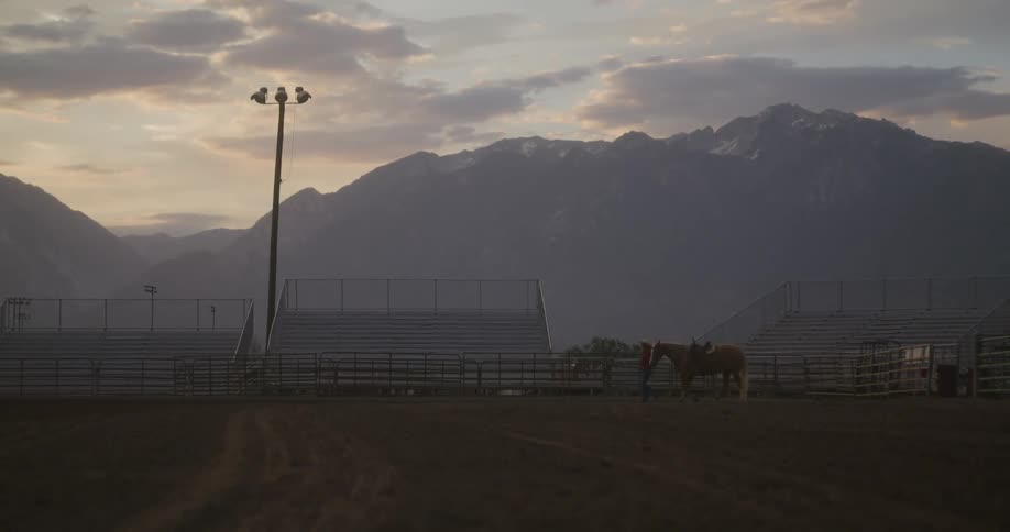 A person walking with a horse behind them on a ranch and a huge mountain behind them