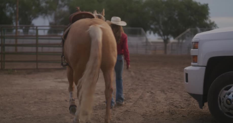 A woman in a cowboy hat walking with a horse at her side on a dirt path