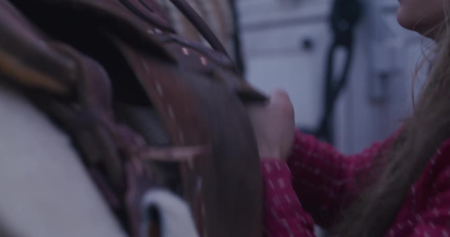 A woman latches the saddle on the horse
