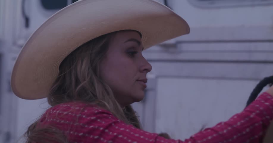 Cowgirl tends a horse next to a trailer