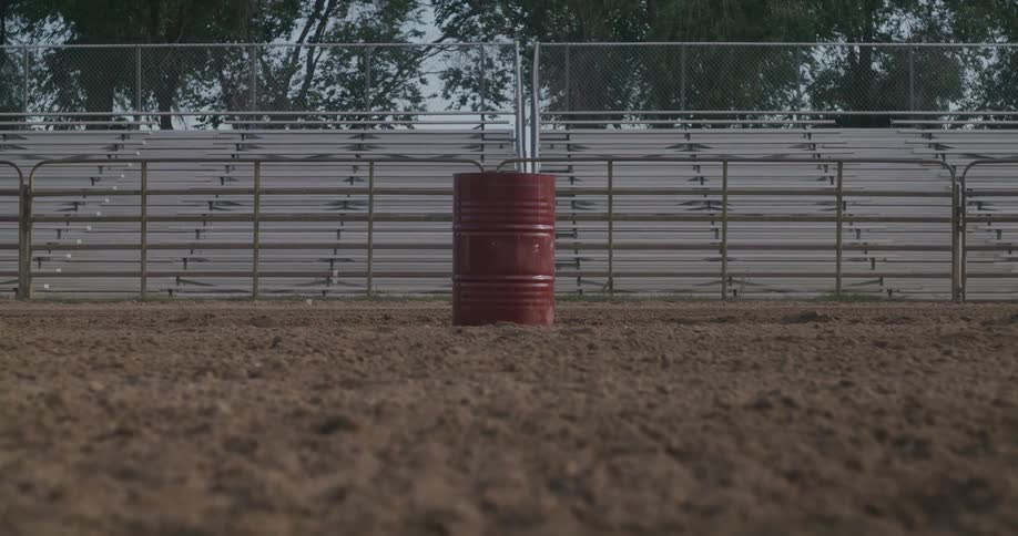 A red barrel on top of the sand and behind it there are fences and a grandstand