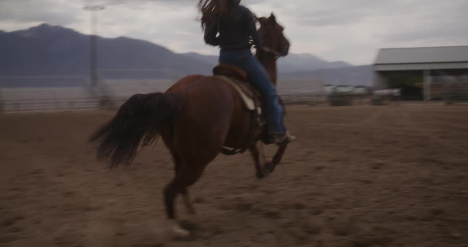 A woman in a cowboy hat gallops on a horse on a farm