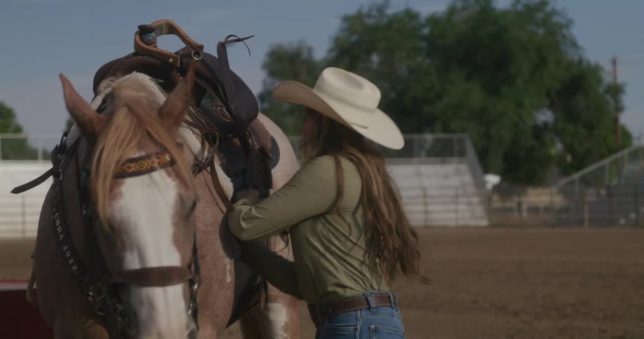Cowgirl adjusting the saddle on her horse