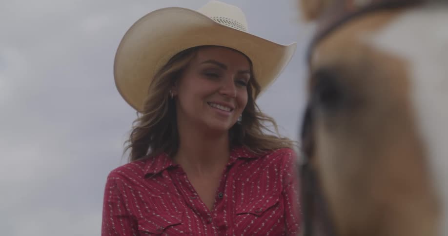 A woman smiling on a horse and wearing a cowboy hat