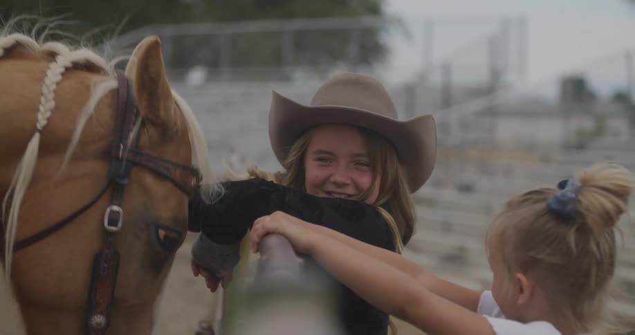 Two little girls are leaning against a fence and smiling and on the other side there is a horse