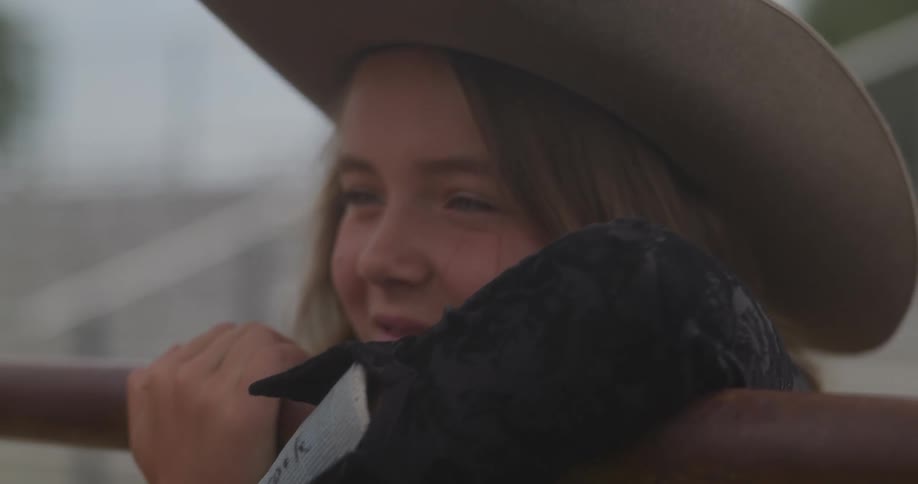 Girl with arm in cast hangs onto rail and strokes horse