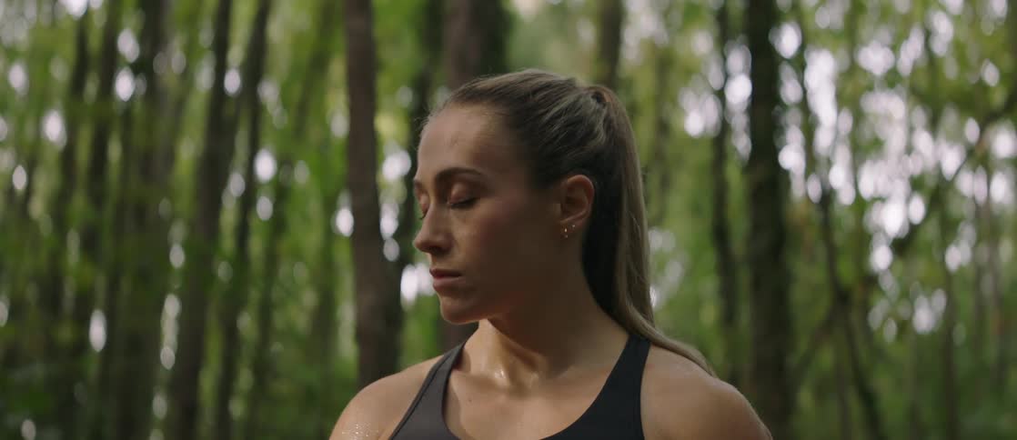 A woman is standing in the woods looking around and then closes her eyes