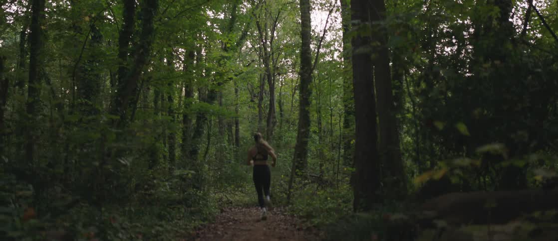 Woman running through a forest facing away