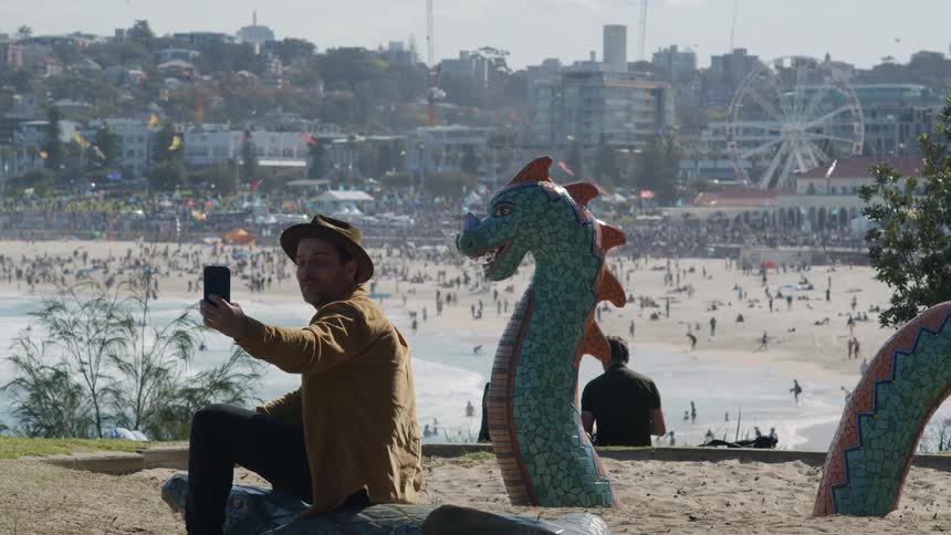 A man taking a selfie with the beach in the background