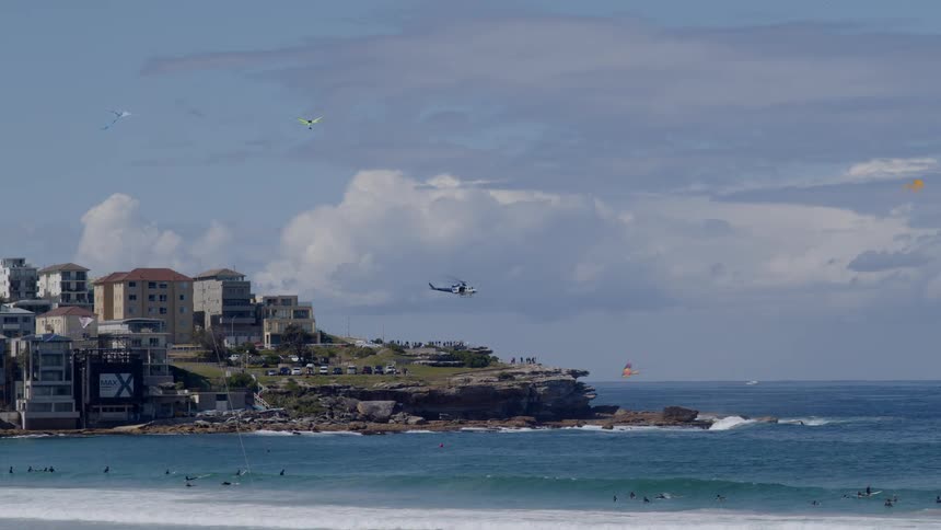 Panorama of a beach with people surfing swimming and a helicopter passing by