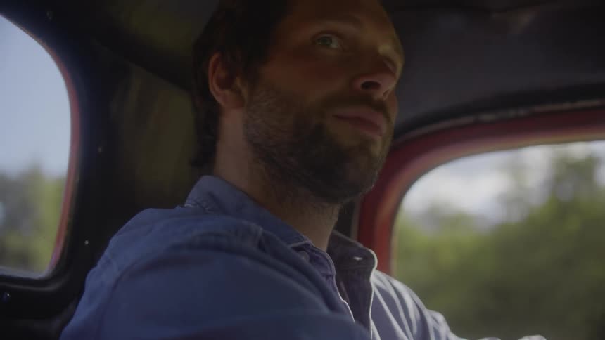 A male farmer drives his red pickup truck across his farm