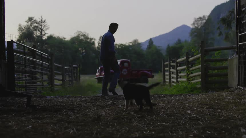 Man walking across his farm towards a pickup truck with his dog accompanying him