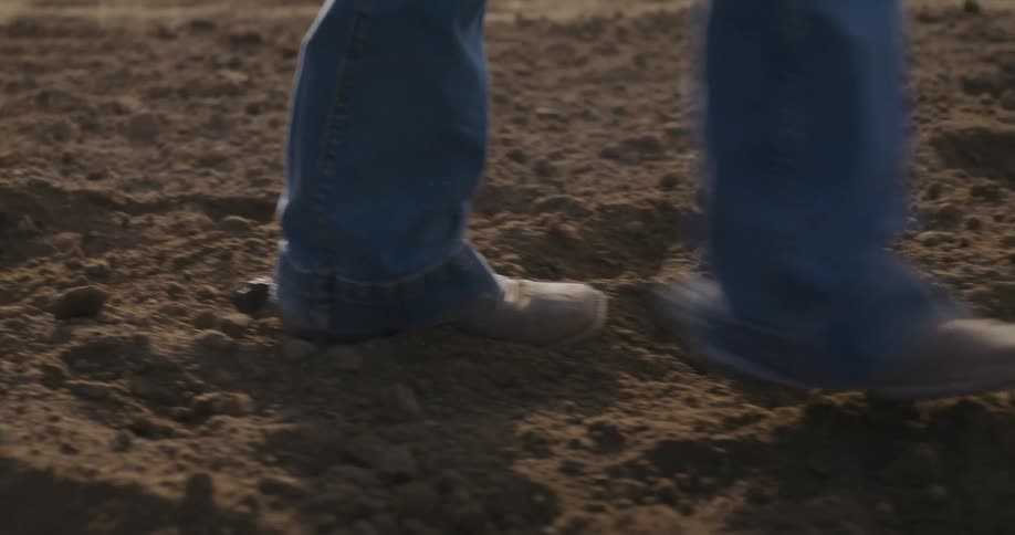 A person wearing jean and boots walking on sand