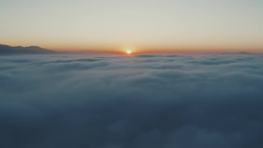 View high above the clouds as the sun glows on the horizon among mountaintops