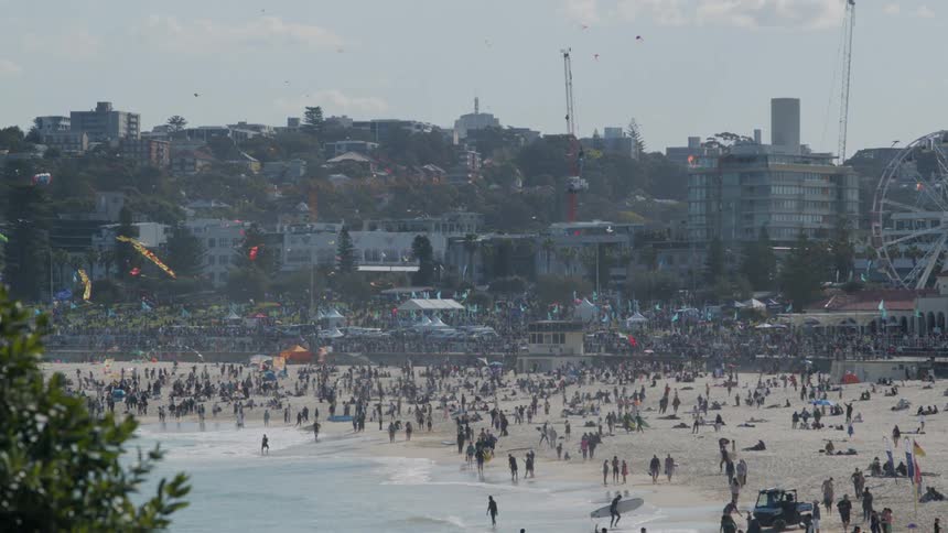 A large crowd of people are on a beach in a city on a sunny day