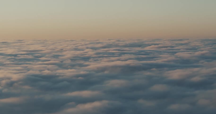 The camera floats above a layer of soft golden clouds at dawn