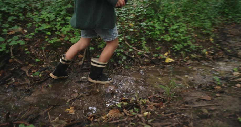 A child with rain boots jumps up and down in a creek