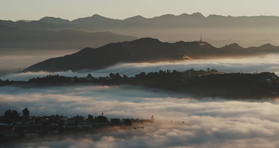 The camera slowly tracks up above the Hollywood Hills as fog rolls through at sunset