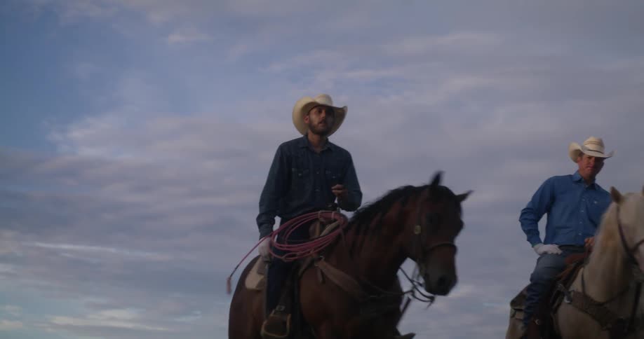 Two men riding horses with one brown and one white