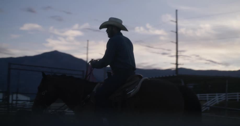 A cowboy riding a horse on a ranch and some cows nearby
