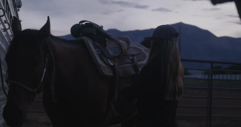 A girl attaching a saddle to a horse