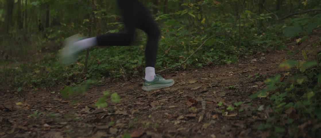 A woman in workout clothes runs up a trail in the forest