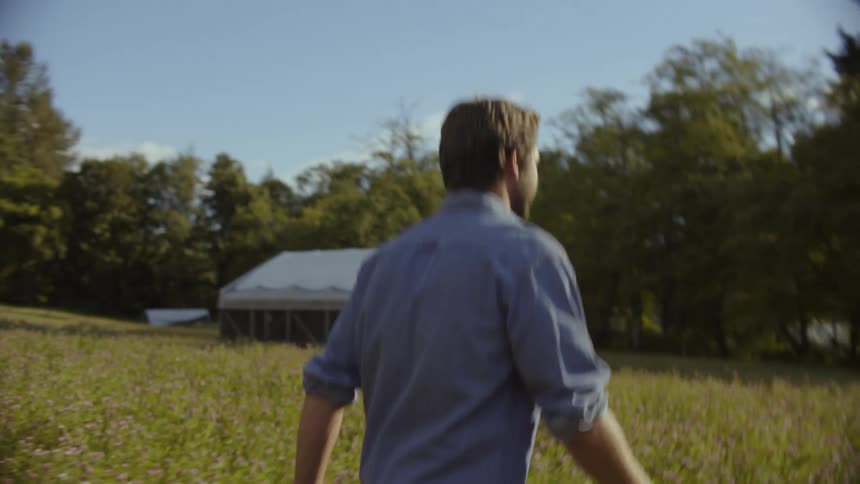 A male farmer walking through a field near a barn
