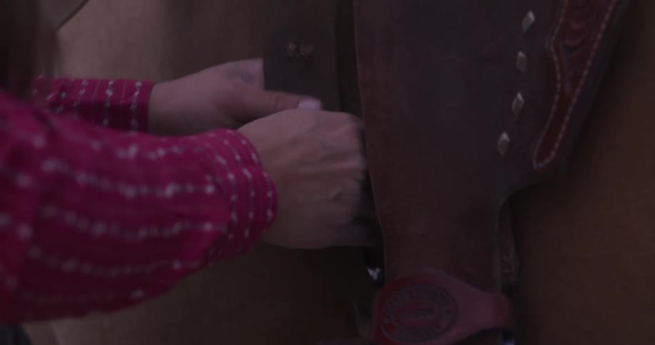 A woman tightens a saddle on a horse