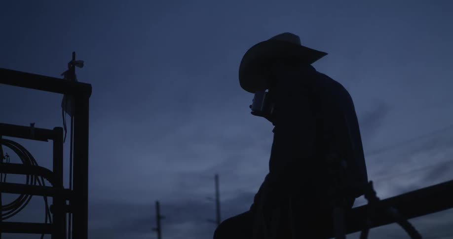 A cowboy sitting alone while drinking coffee from a cup