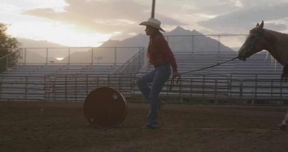 Woman kicking a barrel in a rodeo arena while pulling her horse