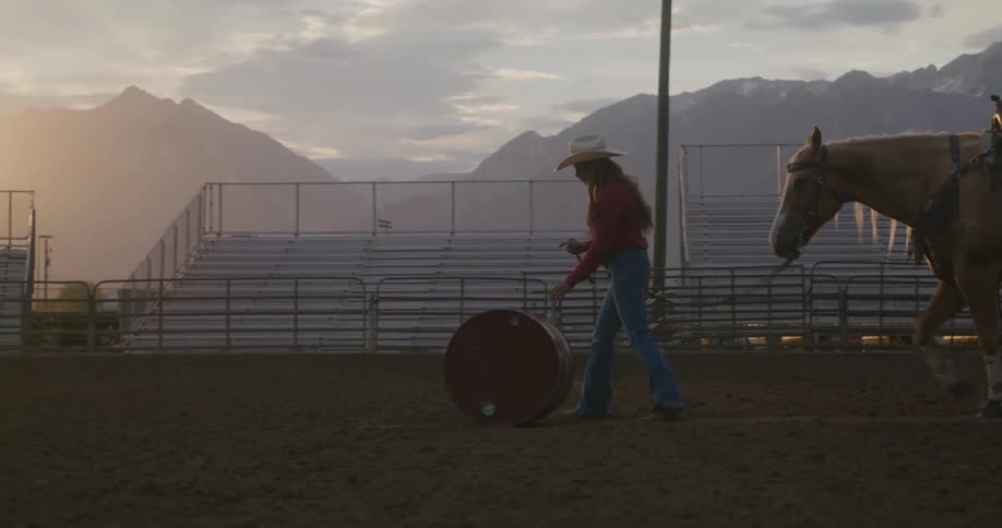 Woman pushing a gallon and standing while pulling her horse at the same time on a rodeo field