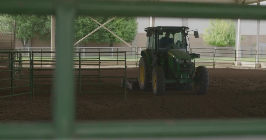 A tractor turns about smoothing the dirt under a covered cattle fence lined show barn
