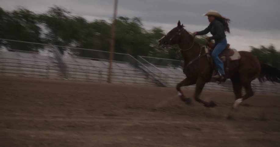 A woman riding a horse running through the dirt arena