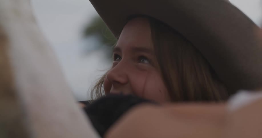 Girl with a cowboy hat smiles next to a horse