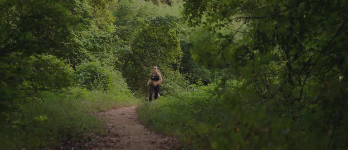 A woman is running hard and fast on a trail out of the woods