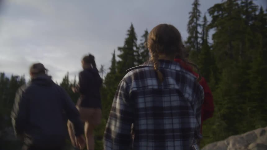 Four teenagers run on a trail towards a body of water surrounded by trees