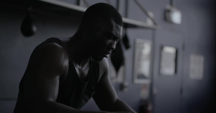 A man sits in a dark gym unwrapping his hands