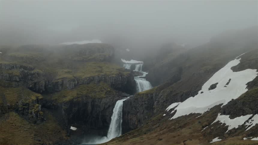 A waterfall pours down the top of a mountain