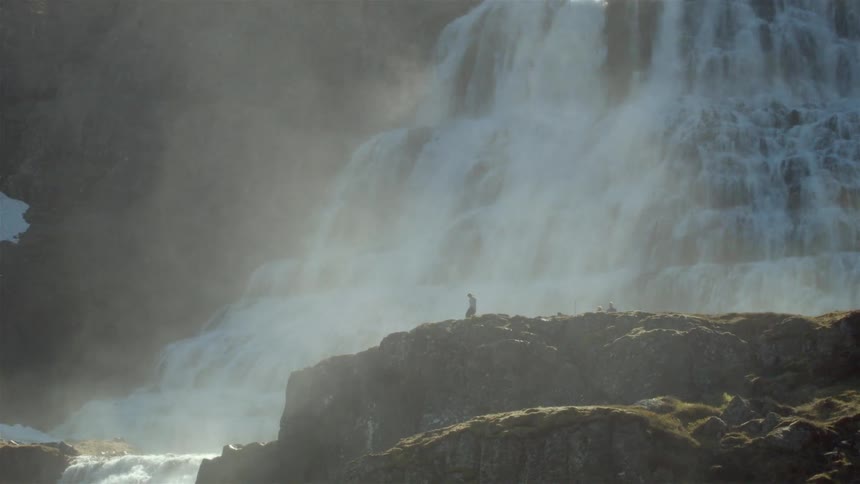 A person is on a cliff near a vast waterfall
