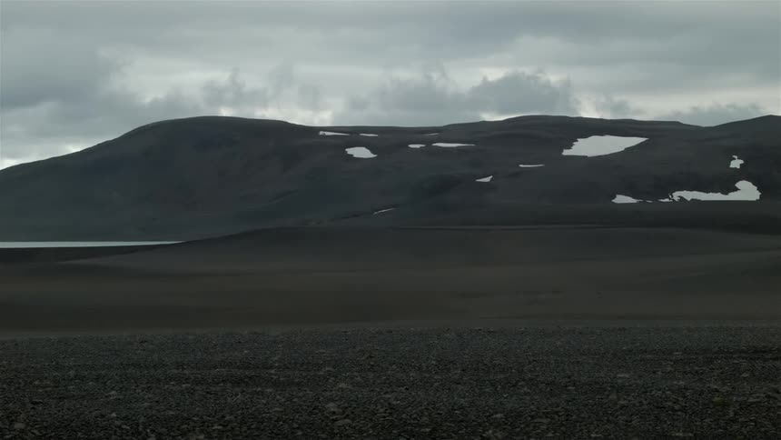 A field leads to a hilly area with some snow on it