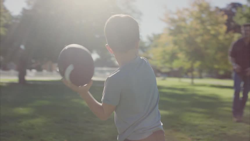 Son throwing an american football to his father in a garden