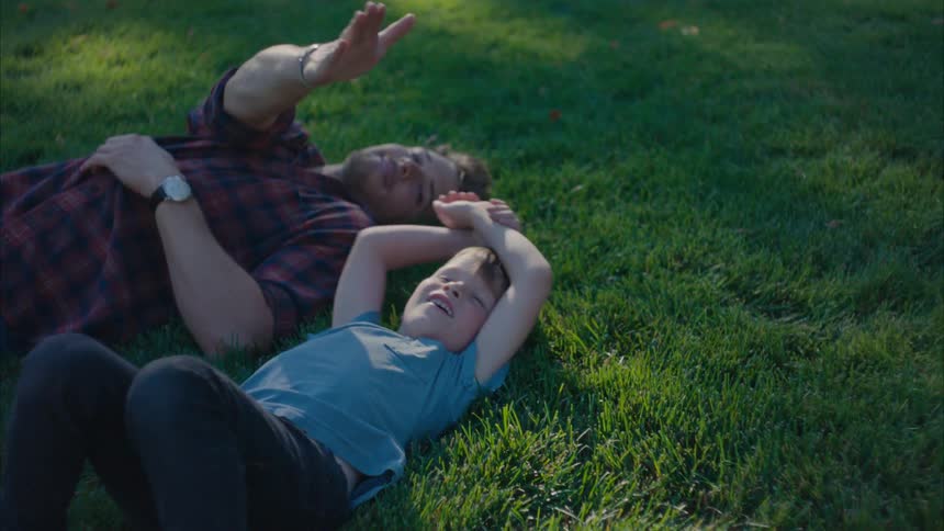 A father and son lay on the grass and throw a football