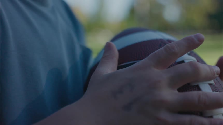 Child with number written on his hand stands in park handling football