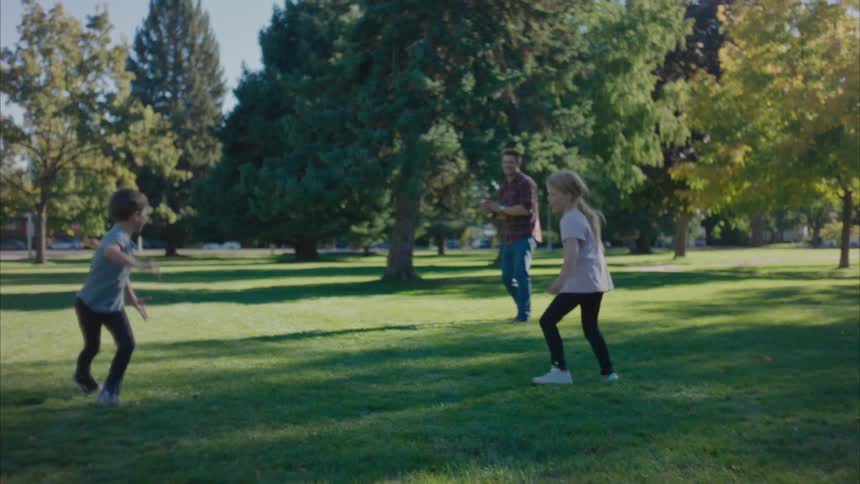 A father and his children playing football in a suburban park