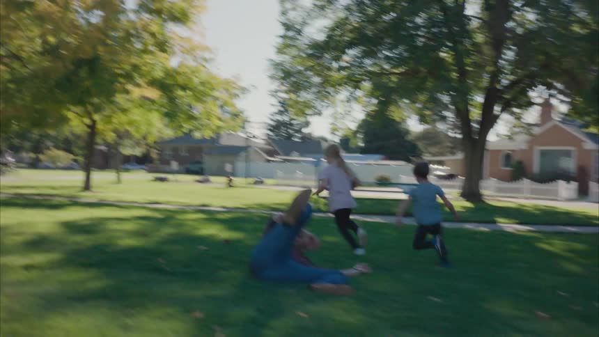 A girl a boy and their father playing american football in a public park